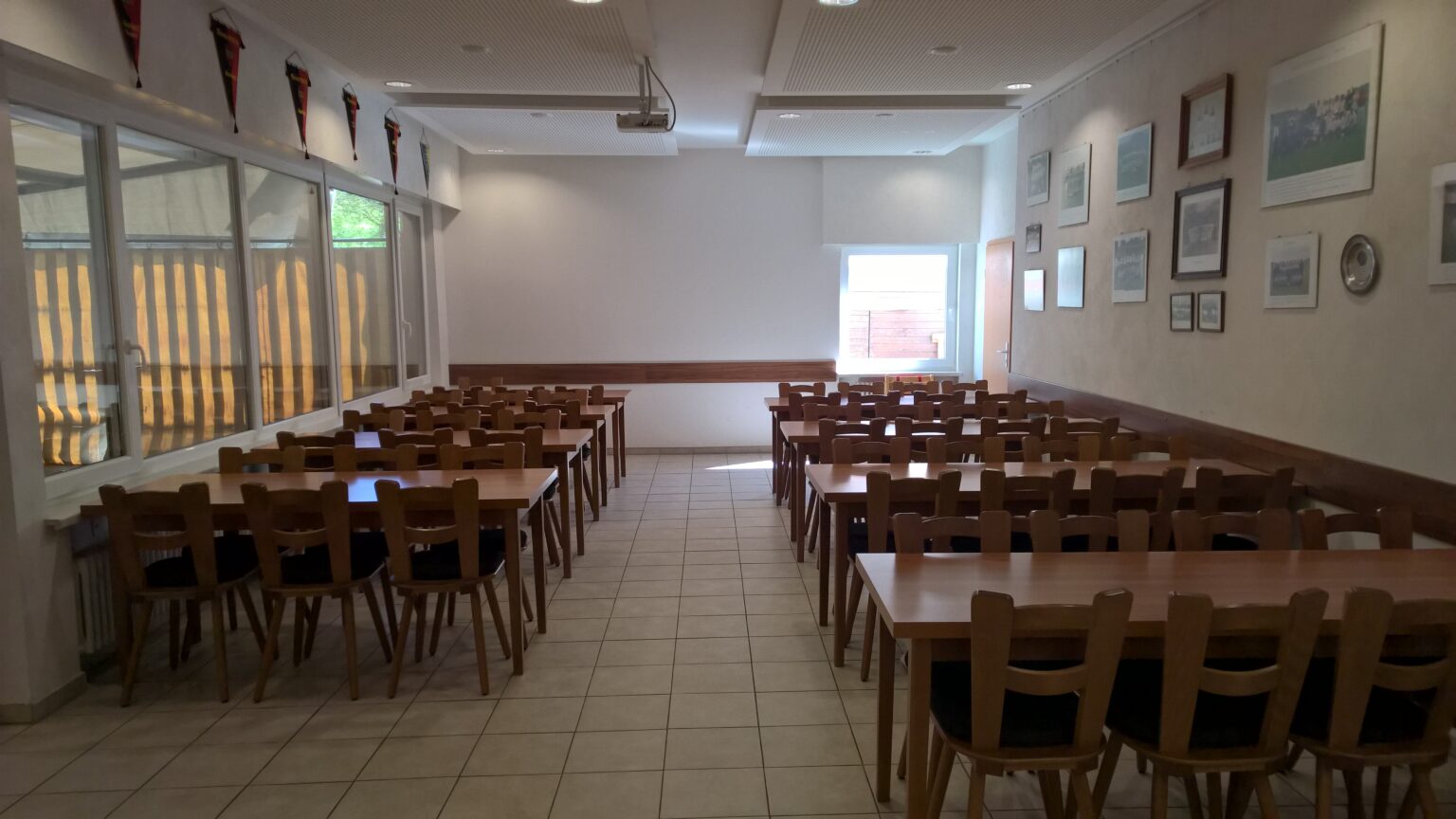 Gastraum des TSV-Vereinsheims mit langen Holztischen und Stühlen, links eine Fensterfront, rechts Mannschaftsfotos an der Wand