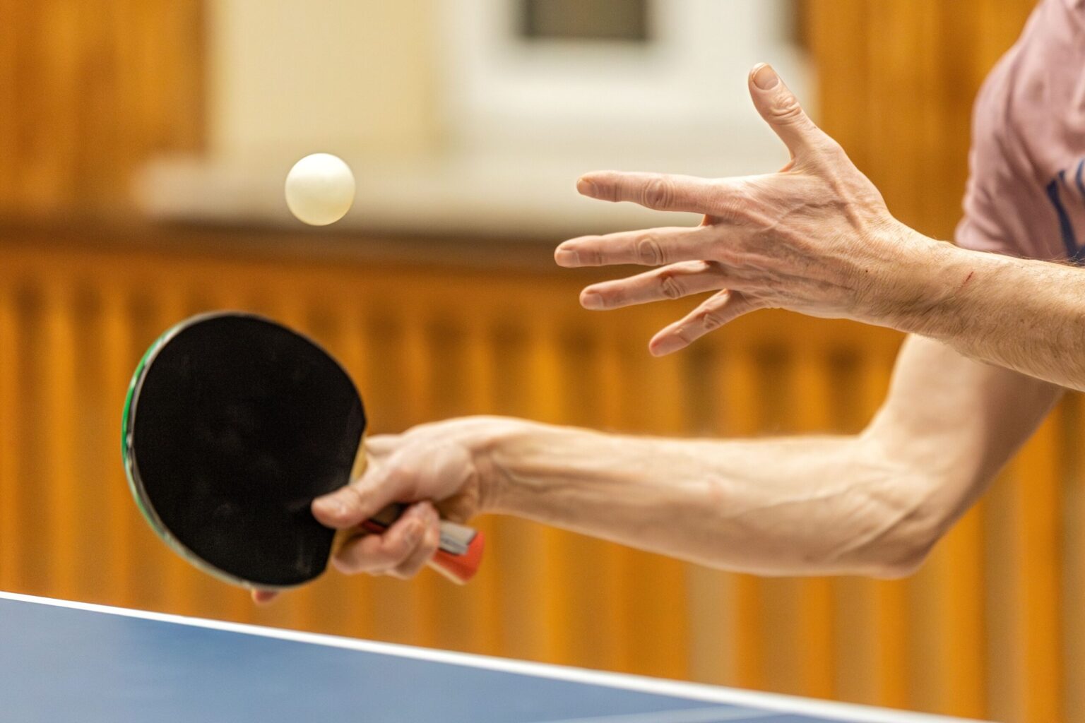 Tischtennisspieler beim Aufschlag: Der Ball schwebt in der Luft, der Schläger ist über der Platte zum Schlag ausgeholt